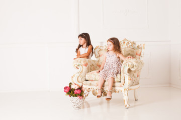 Two girls sits in a magnificent ancient armchair 