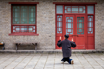 un homme chinois habillé en noir, s'entraine à un art martial seul dans un décors asiatique