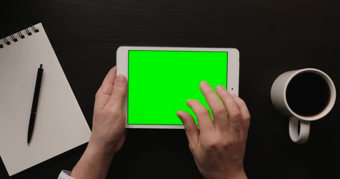 Business man using tablet, checking information on tablet with green screen. Hands top view. Office desk background. Slow motion. Top view. Chroma key. Close up.
