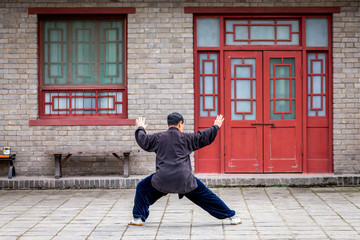 un homme chinois habillé en noir, pratique un art martial seul dans un décors asiatique