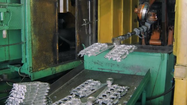 robotic arm is throwing cooled metallic details for car engine in a automobile factory