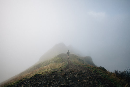 Man Walking Towards Mountain Peak In Foggy Weather