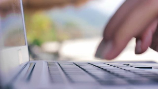 Close up of woman's hands typing on a laptop computer outdoors. Woman freelancer working with laptop sitting at table on the beach