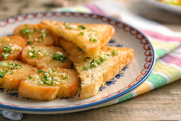 Plate with tasty garlic French bread slices on wooden table