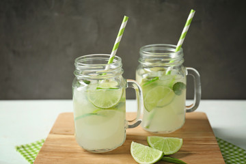 Glass jars of bracing cocktail with lime slices on wooden board against dark background