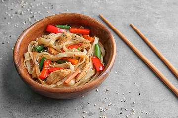 Wooden plate with delicious rice noodle and vegetables on grey background
