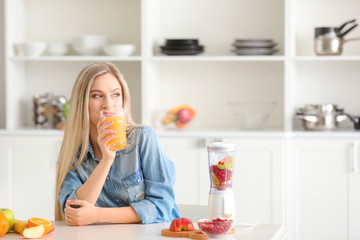 Beautiful young woman drinking fresh juice in kitchen