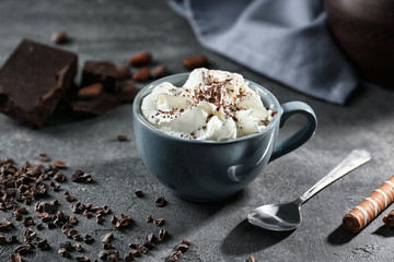 Cup of delicious cocoa drink with whipped cream on grunge kitchen table