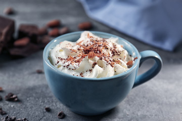 Cup of delicious cocoa drink with whipped cream on grunge kitchen table