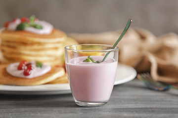 Glass of yogurt with mint leaves on table against blurred background