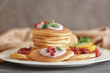 Stack of pancakes on plate with yogurt, cranberry and mint leaves against blurred background