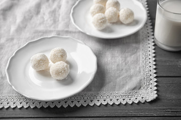 Plates with tasty candies in coconut flakes on wooden table