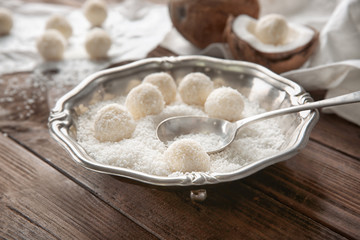 Plate with tasty candies in coconut flakes on wooden table