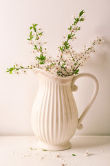 Jug with blossoming spring branches on table