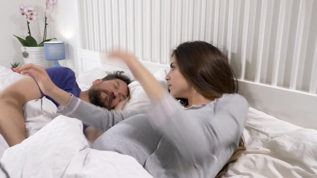Dolly shot of pregnant woman with contractions in bed trying to wake up sleeping husband