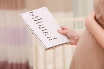 Pregnant woman holding list of baby names in notebook at home