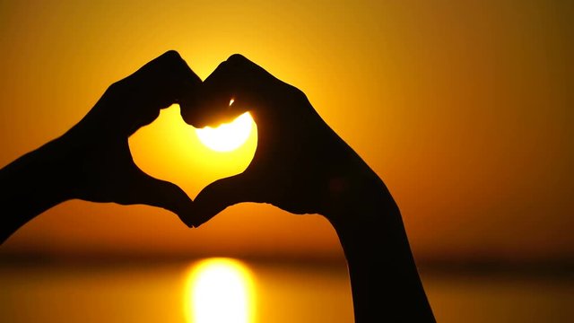 Woman makes heart and hands directs the sunset