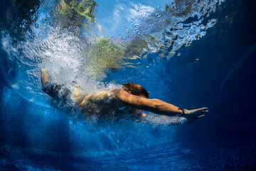 Obraz na płótnie Canvas Underwater shot of the young man jumping in the pool