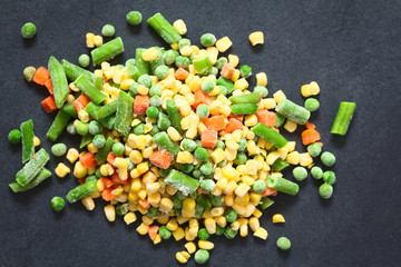 Frozen mixed vegetables (green bean, pea, carrot, sweet corn) photographed overhead on slate with natural light (Selective Focus, Focus on the vegetables on the top)