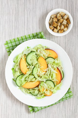 Fresh nectarine, cucumber and iceberg lettuce salad on plate with homemade croutons on the side, photographed overhead with natural light