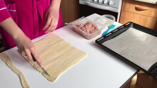 Stages of preparation of meat glomeruli. A woman slices thin strips of dough. Next to the table is a stuffing and lie tools. Video shot on the iPhone 7 Plus.