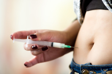 Woman with syringe make a subcutaneous abdomen injection of insulin to her belly - diabetes concept