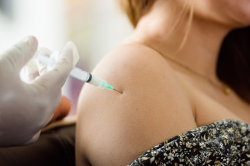 Nurse with syringe make an injection to a woman's shoulder