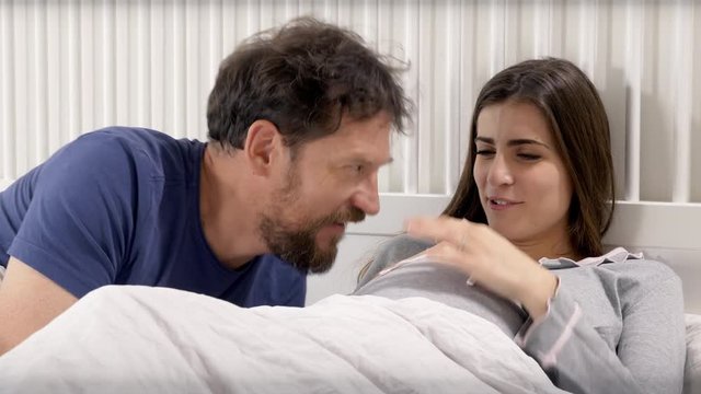 Happy man and woman in bed expecting baby talking closeup