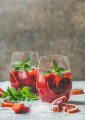 Blood orange and strawberry summer Sangria. Fruit refreshing rose wine cocktails in glasses with ice and mint leaves, dark background, vertical composition, copy space