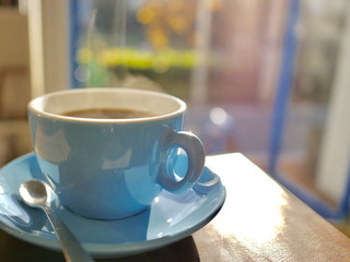hot black coffee in light blue cup on wooden table, warm and cozy atmosphere cafe, aroma smell from cup