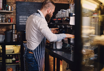 Bearded male is making coffee in a coffee shop.