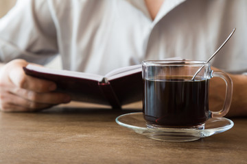 Man drinking black coffee at the table in the cafe and reading a book at lunch time. Coffee break.