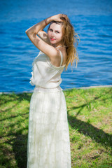 Fototapeta na wymiar Young blond head European woman with pale skin in stylish pastel vintage lace dress and pearl jewelry on nature near garden and water