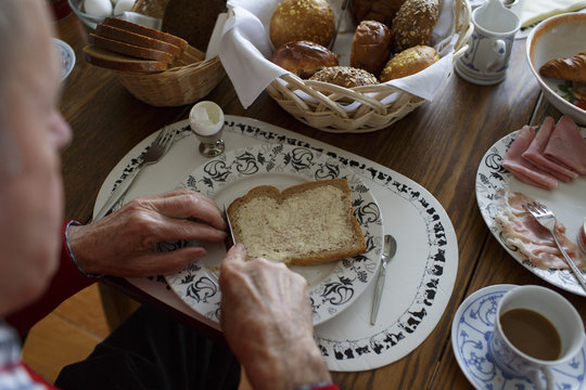 hands of an older man putting butter on a slice of bread