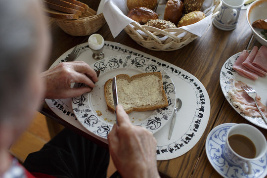 hands of an older man putting butter on a slice of bread