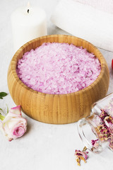 Fototapeta na wymiar Bath salt with aroma of a rose in a wooden bowl, petals and a fresh pink rose, towels and candles on a white background
