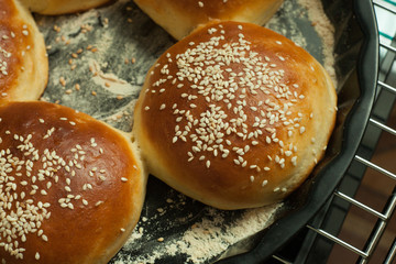 home bake buns for burgers with sesame in a baking form on black background, top view