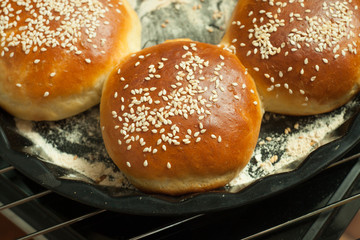 buns for burgers with sesame in a baking form on black background, top view