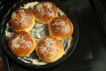 buns for burgers with sesame in a baking form on black background, copy space