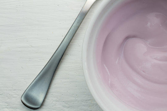Creamy naturally colored rasberry fruit yogurt in white glass bowl with spoon close up top view photograph