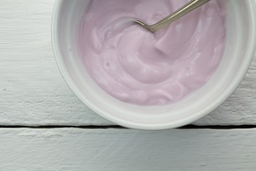 Creamy naturally colored rasberry fruit yogurt in white glass bowl on white wood table close up with spoon -  top view photograph