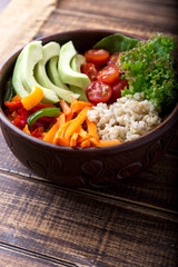 Vegan buddha bowl on wooden background. Bowl with carrot, lettuce, tomatoes cherry, pepper, avocado and porridge. Vegetarian, healthy, detox food concept.