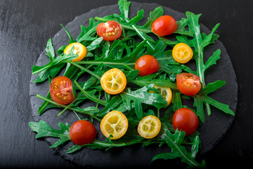 Fresh arugula salad with kumquat and tomato cherry on slate plate. Top view. Healthy food. Diet.