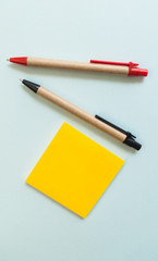Pens and yellow post note on blue background, view from above