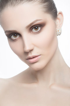 Portrait of young beautiful female with evening makeup and earrings looking at camera on white background.