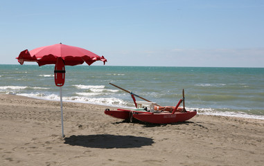 Pattino rosso di salvataggio e ombrellone sulla spiaggia di sabbia