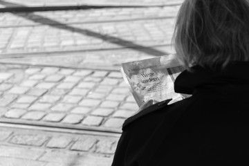Blick über den Rücken einer älteren Frau die gerade eine Zeitung liest mit dem Titel, Wege ins jetzt, und Bahngleise im Hintergrund - obrazy, fototapety, plakaty