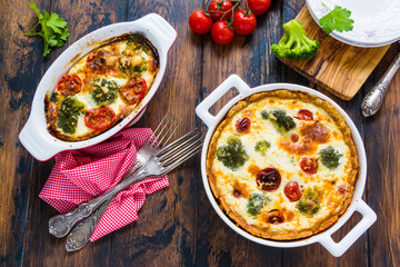 Homemade quiche with broccoli and cherry tomatoes in the baking dishes on the rustic wooden table, top view.