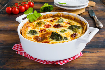 Vegetarian broccoli and tomatoes pie in a white casserole on the wooden rustic table.