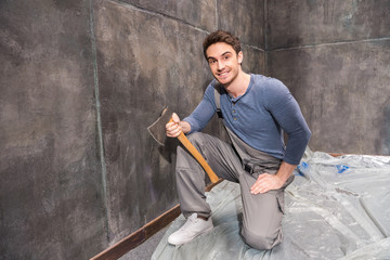 Fototapeta na wymiar Professional young handyman with axe repairing floor, renovation concept